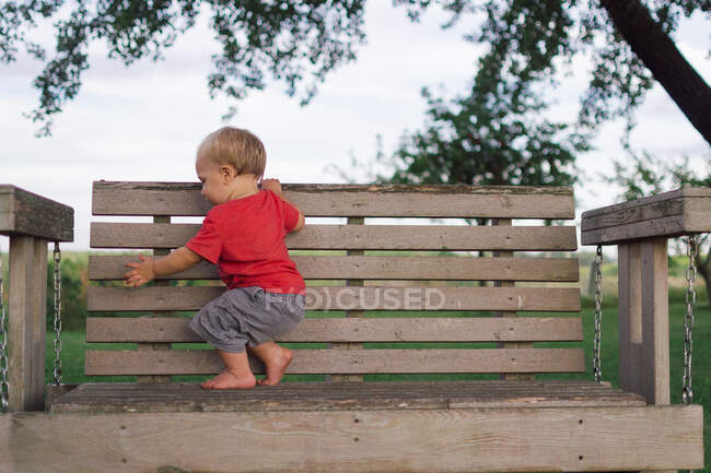 Garçon grimpant sur un banc en bois sur la nature — Photo de stock