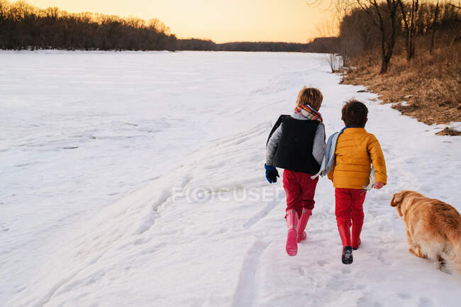 Deux garçons et un chien courant sur une rivière gelée dans la soirée — Photo de stock