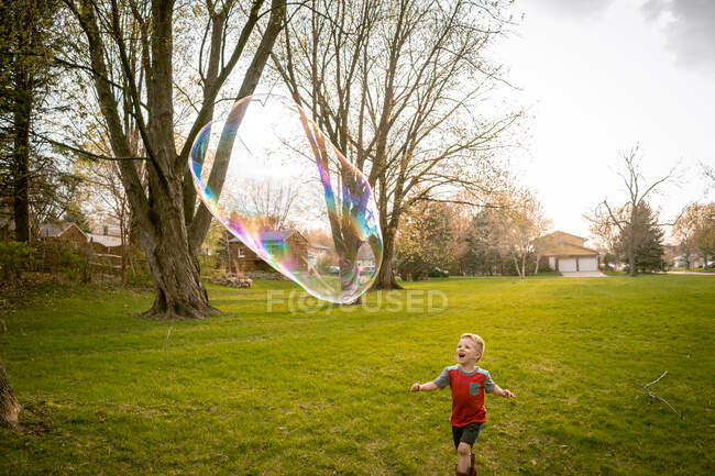 Хлопчик переслідує гігантську мильну бульбашку — стокове фото