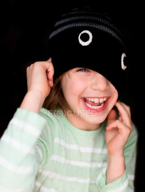 Портрет мальчика, смеющегося, натягивающего шапочку на лицо — стоковое фото