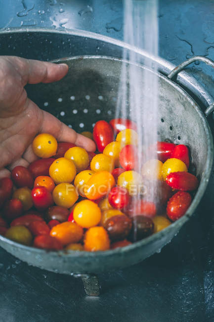 Mann wäscht Kirschtomaten im Sieb — Stockfoto