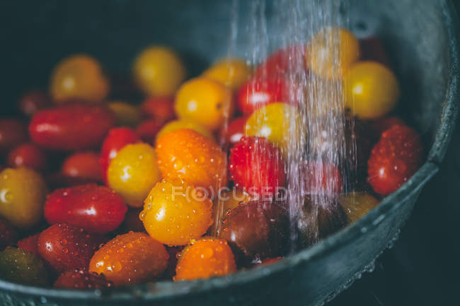 Черри помидоры в дуршлаге под проточной водой — стоковое фото