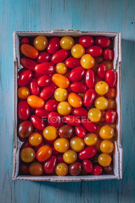 Vista superior de la caja de tomates cherry sobre la mesa azul - foto de stock