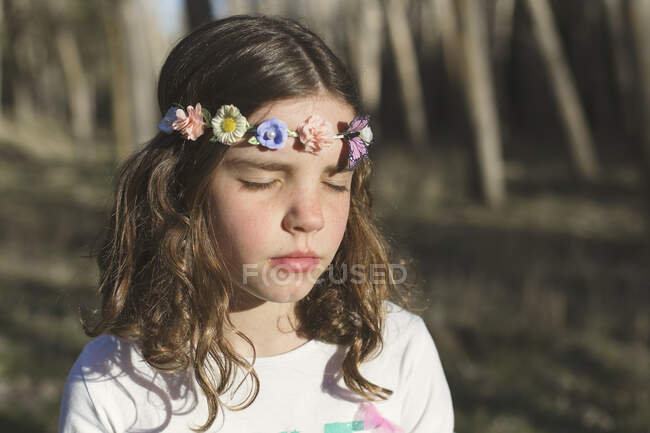 Retrato de una niña con los ojos cerrados con una corona de flores en la cabeza - foto de stock