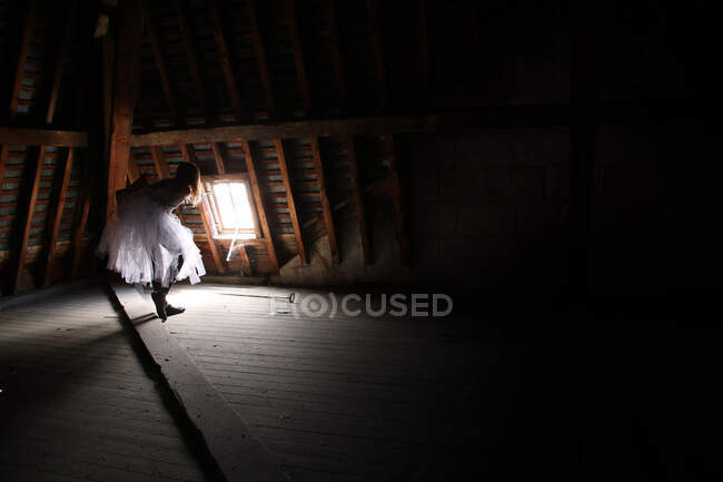 Teenage girl looking through a skylight in the attic — Stock Photo