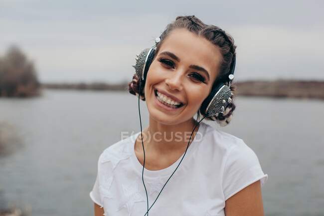 Retrato de uma mulher sorrindo usando fones de ouvido cravados — Fotografia de Stock