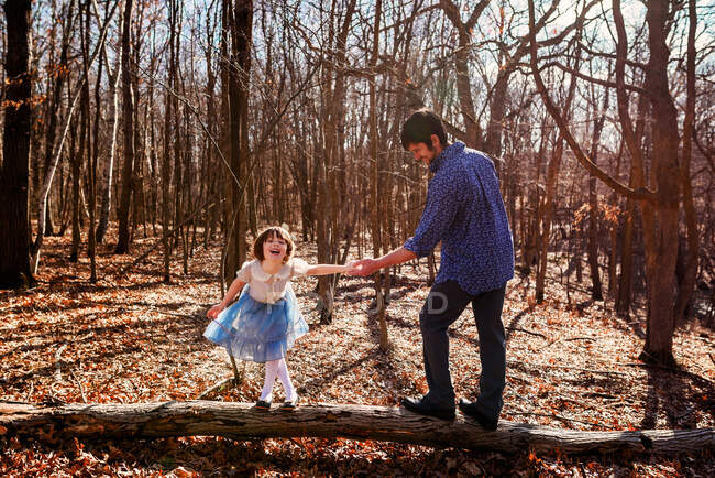 Padre e hija de pie sobre un tronco de árbol en el bosque - foto de stock