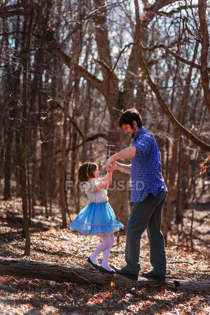Padre e hija tomados de la mano de pie sobre un tronco de árbol en el bosque - foto de stock