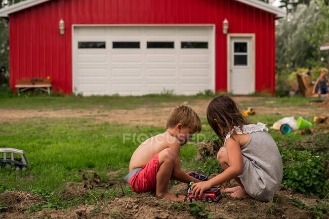 Chico y chica jugando en la tierra con un chico en el fondo - foto de stock