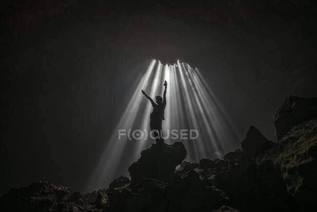 Silhouette di un uomo in piedi in una grotta con le braccia alzate, Jomblang, Giava centrale, Indonesia — Foto stock