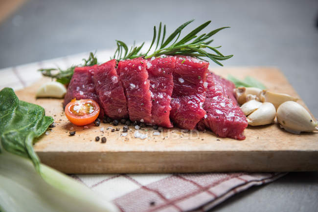 Closeup view of raw steak with tomatoes, garlic and herbs — Stock Photo