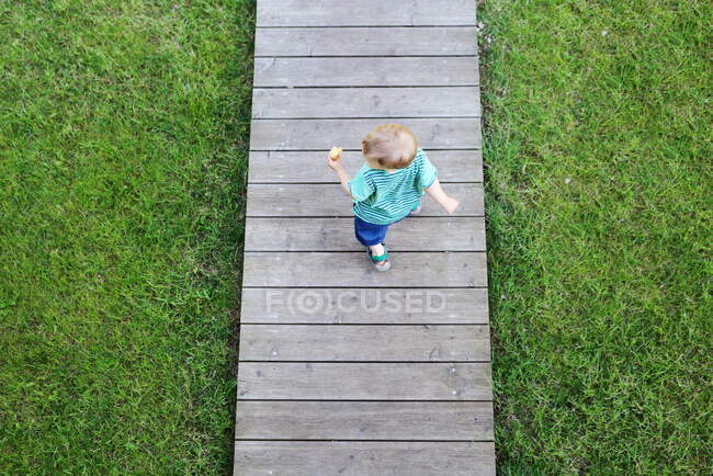 Blick aus der Vogelperspektive auf einen Jungen, der auf einer Holzpromenade läuft — Stockfoto