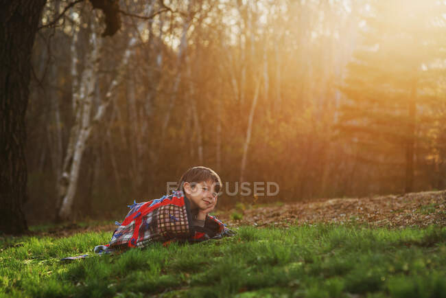 Хлопчик лежить на траві, загорнутий у ковдру на сонці — стокове фото