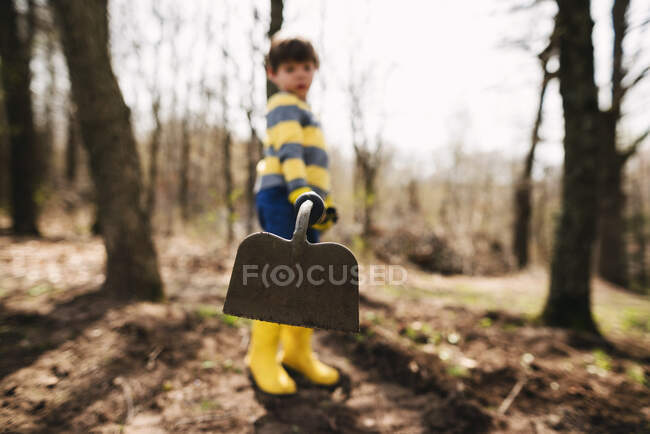 Niño de pie en el jardín con una azada - foto de stock