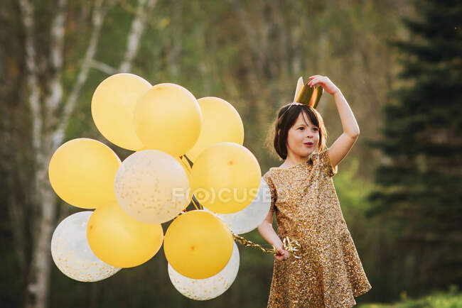 Chica en un vestido de oro con una corona que lleva globos - foto de stock
