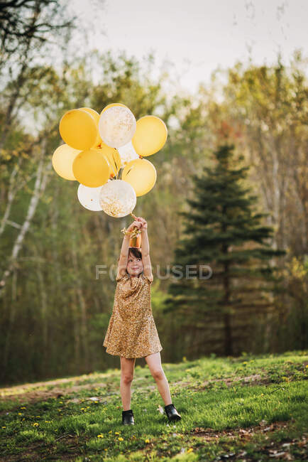Chica en un vestido de oro con una corona que lleva globos - foto de stock