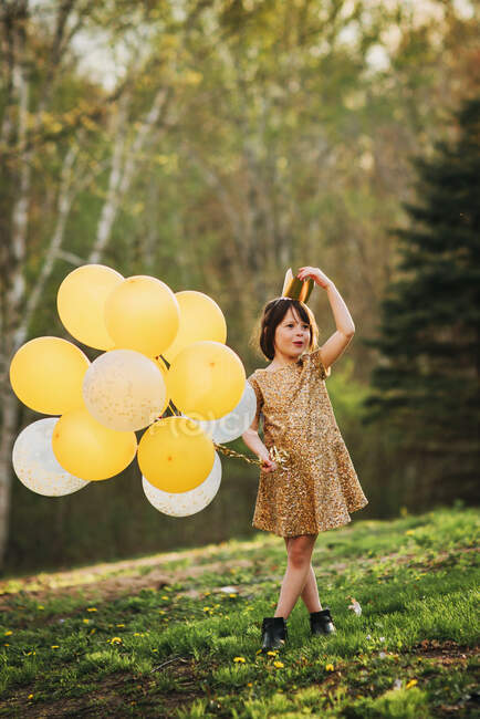 Girl in a gold dress wearing a crown carrying balloons — Stock Photo