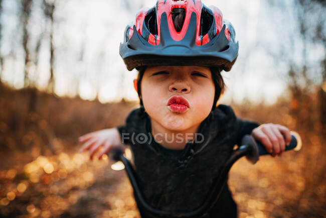 Niño en una bicicleta con un casco labios fruncidos - foto de stock