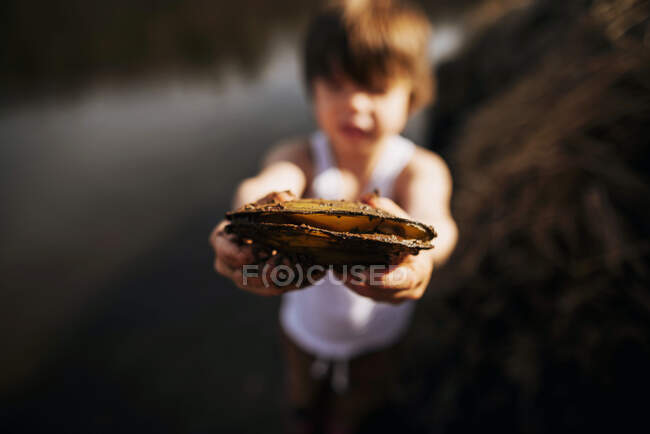 Niño en la playa sosteniendo una almeja - foto de stock