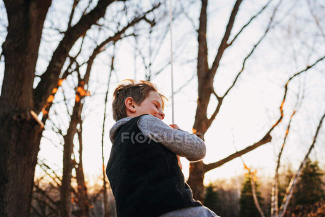 Menino balançando em um balanço de corda no pôr do sol outonal — Fotografia de Stock