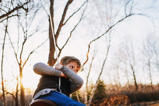 Niño balanceándose en un columpio de cuerda en la puesta de sol otoñal - foto de stock