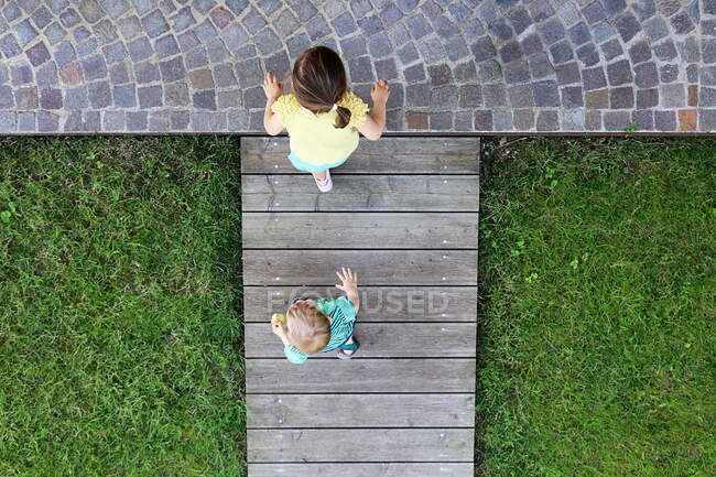 Vista aérea de un niño y una niña caminando sobre un malecón de madera - foto de stock