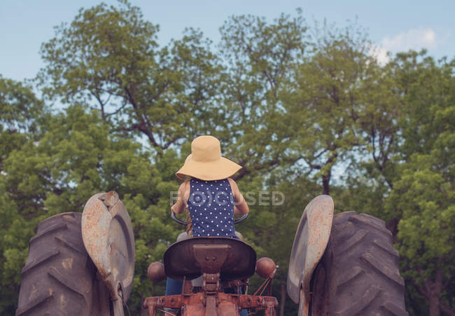 Visão traseira de uma menina sentada em um trator — Fotografia de Stock