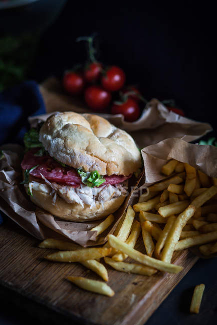 Tasty fish burger with potato fries over chopping board — Stock Photo