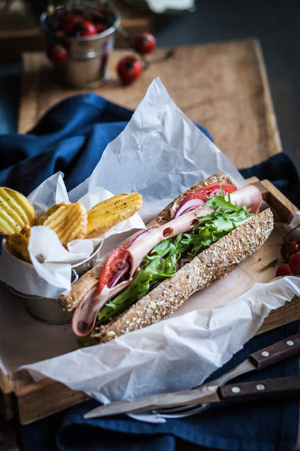 Ham sandwich and potato fries wrapped paper — Stock Photo