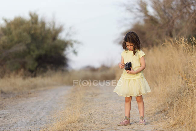Menina de pé em uma estrada rural segurando uma câmera vintage, Andaluzia, Espanha — Fotografia de Stock