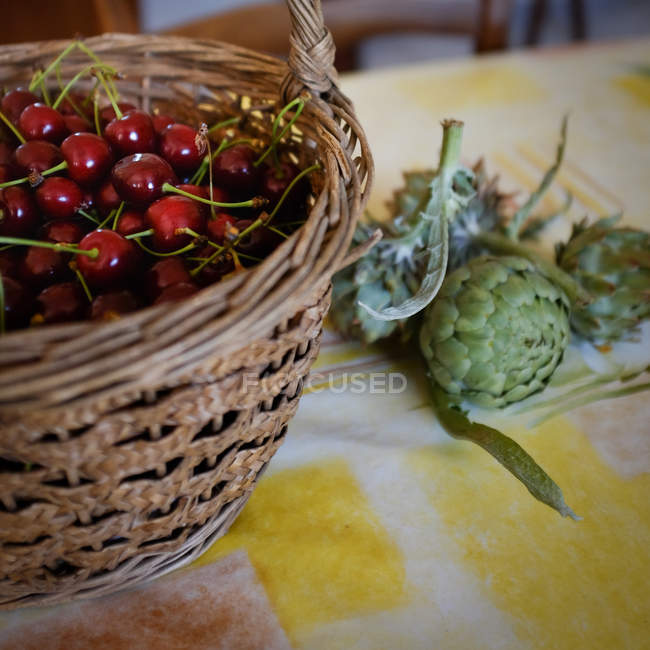 Wicker basket with cherries and artichokes closeup — Stock Photo