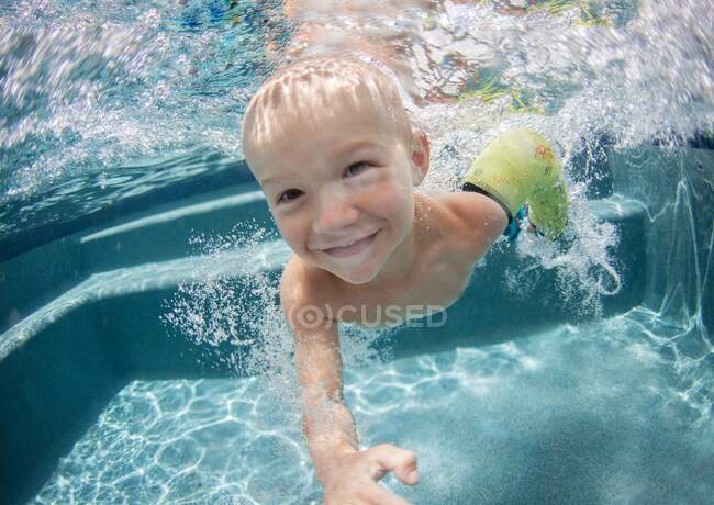 Garoto sorrindo usando um gesso em seu braço nadando debaixo d 'água — Fotografia de Stock