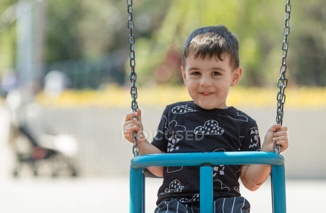 Мальчик сидит на качелях на детской площадке — стоковое фото