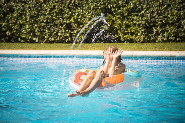 Мальчик сидит на надувном резиновом кольце в бассейне, уклоняясь от потока воды — стоковое фото