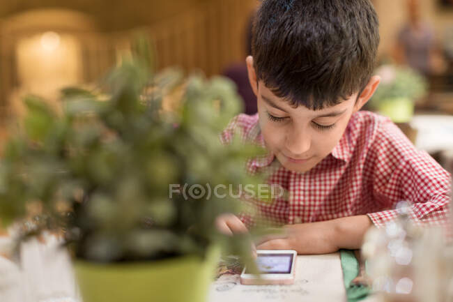 Хлопчик сидить у ресторані, грає в гру на своєму мобільному телефоні — стокове фото