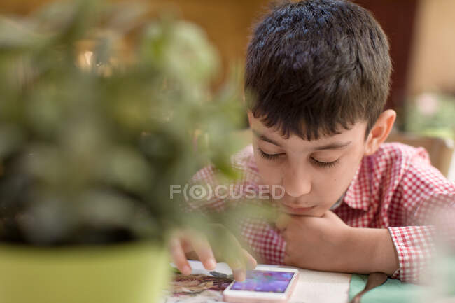 Мальчик, сидящий в ресторане и играющий в игру на мобильном телефоне — стоковое фото