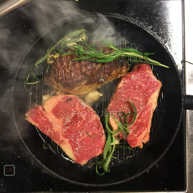 Tasty juicy steaks frying in a frying pan — Stock Photo