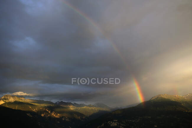 View of mountains with beautiful rainbow in cloudy sky — Stock Photo