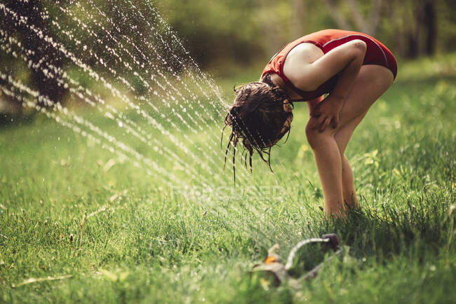 Девушка играет в разбрызгивателе на заднем дворе — стоковое фото
