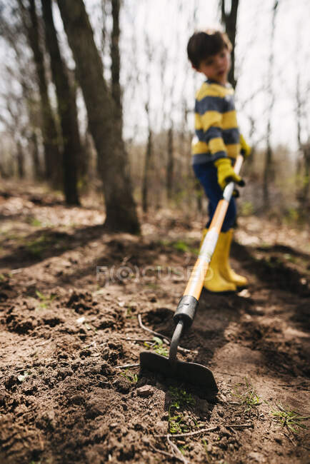 Rapaz a cavar o solo com uma enxada — Fotografia de Stock