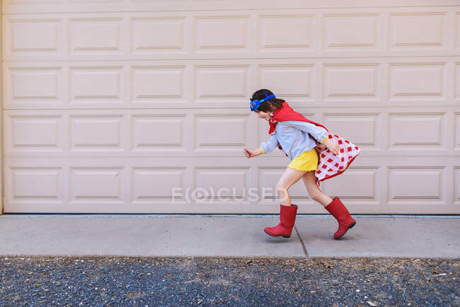 Девушка бежит мимо гаражной двери одетый как супергерой — стоковое фото