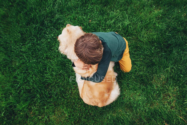Vue aérienne d'un garçon embrassant son chien golden retriever — Photo de stock