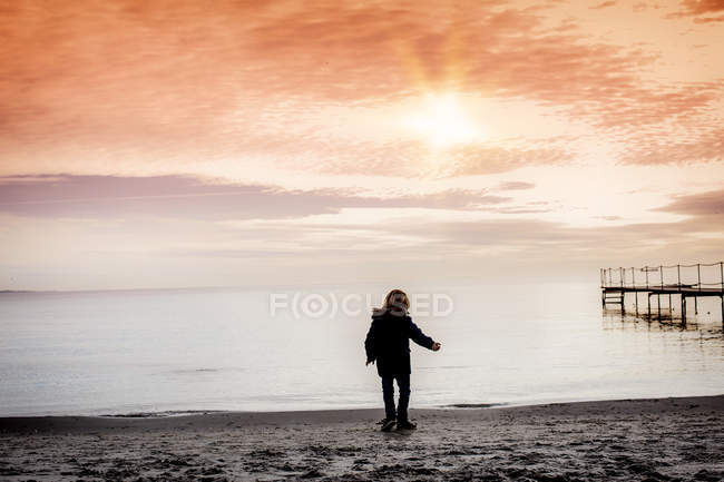Vista trasera Niño en la playa lanzando guijarros en el mar, Dinamarca - foto de stock