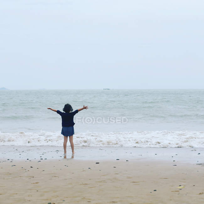 Ragazza in piedi sulla spiaggia vicino all'oceano con le braccia tese, Zhoushan, Cina — Foto stock