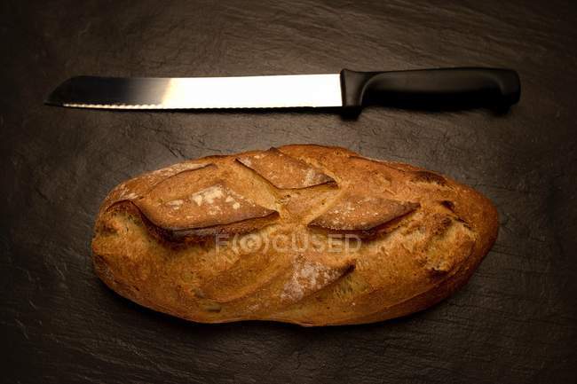Loaf of bread with a bread knife over table — Stock Photo