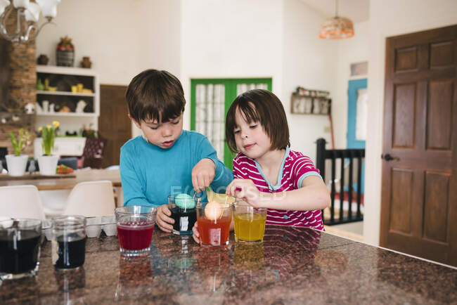 Garçon et fille debout dans la cuisine mourant oeufs de Pâques — Photo de stock