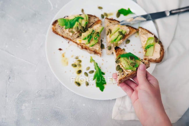 Woman hand holding avocado and brie toast — Stock Photo