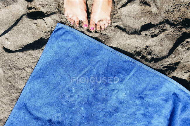 Primer plano de los pies de una mujer en la arena por una toalla de playa - foto de stock