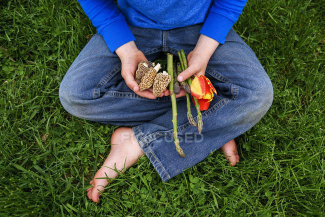 Хлопчик сидить на траві тримає свіжі овочі — стокове фото