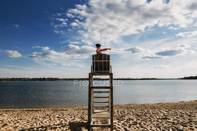 Chica de pie en una silla salvavidas junto a un lago señalando - foto de stock